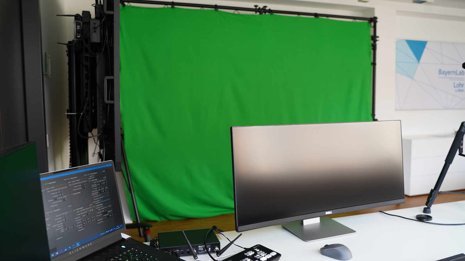 Foto zeigt mehrere Monitore und Aufnahme-PCs, sowie einen Green-Screen. Hier werden die Aufnahmen für Livestreams für BayernLab Online aus Lohr am Main gemacht.